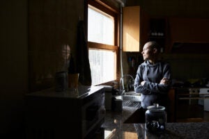 Hairless woman portrait at home looking through the window with folded arms waiting for coffee.