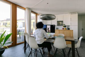 A hispanic woman doctor talking to a female patient via video from home. The doctor is sitting in a bright and beautiful apartment with ample natural light, the patient is pointing at pain behind the ear.