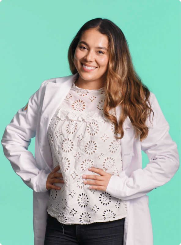 Woman wearing lab coat standing with hands on hips smiling