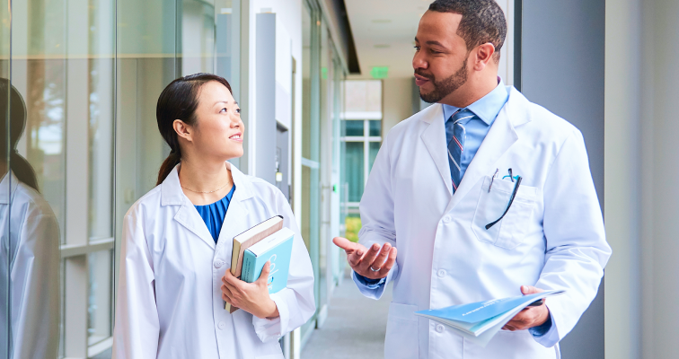 Woman and man wearing lab coats talking to eachother as they walk