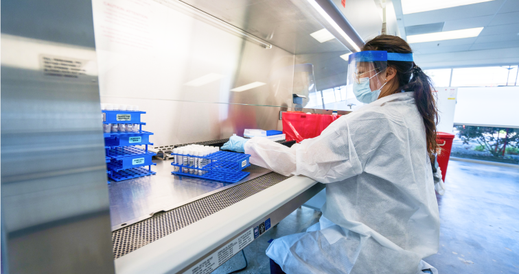 Woman in a lab wearing face mask and mask processing samples in test tubes