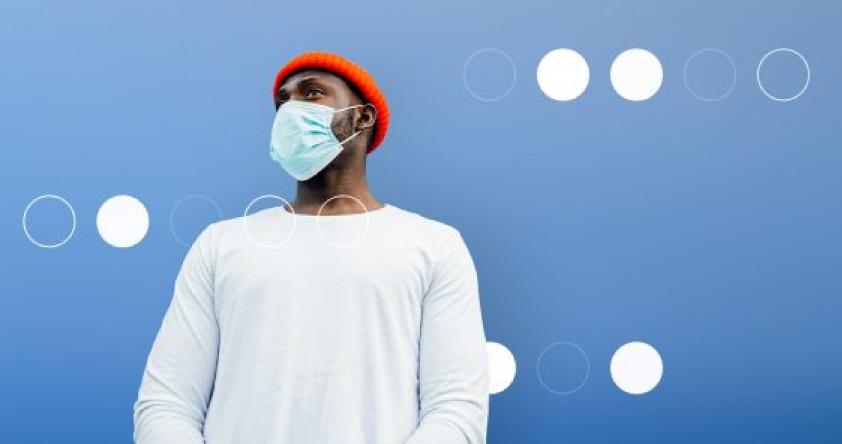 Man wearing mask an red beanie standing in front of blue background