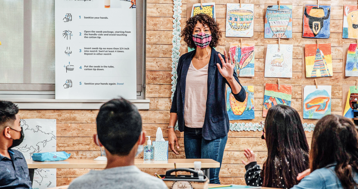 Image of smiling teacher waving to classroom full of students.